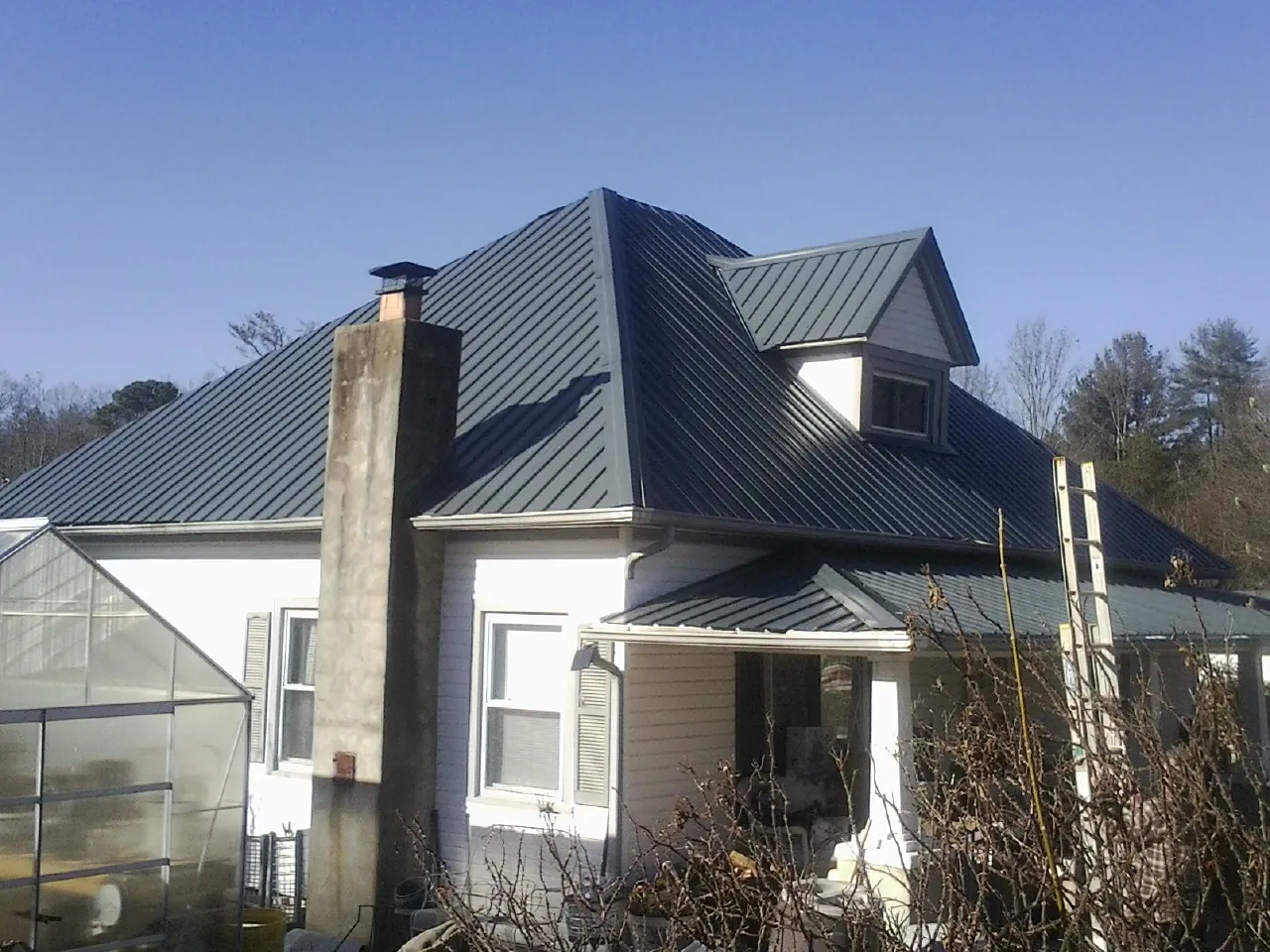Dark blue standing seam metal roof on a white farmhouse with dormer — Slate & Tile Roof Repair by Roofing Brothers in La Plata