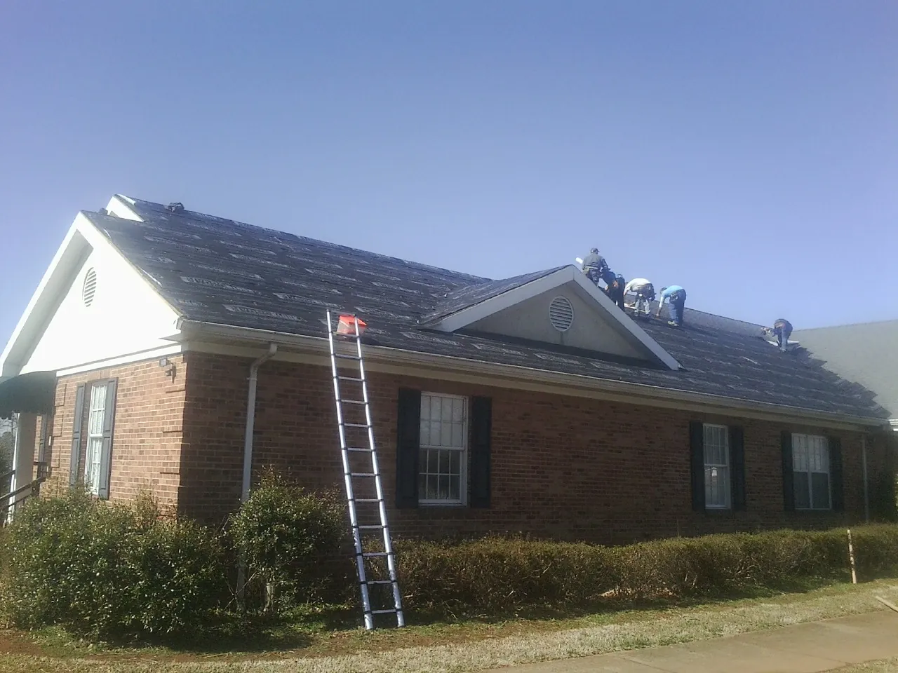 Crew tearing shingles off a brick ranch roof with a ladder set — Emergency Roof Repair work by our crew in La Plata