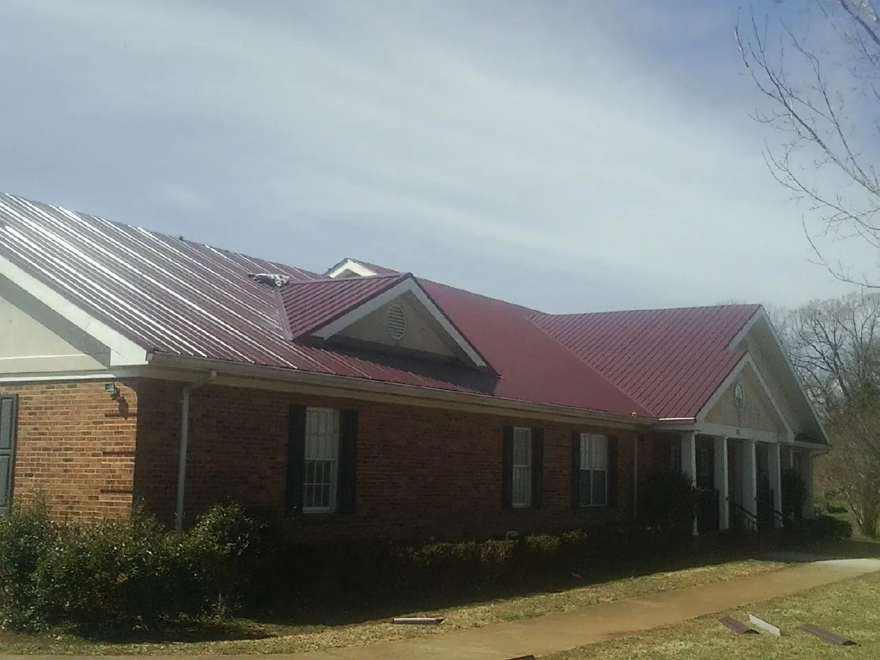 Red metal roof with gabled entries on a long brick building, from a Hail Damage Roof Repair job in La Plata