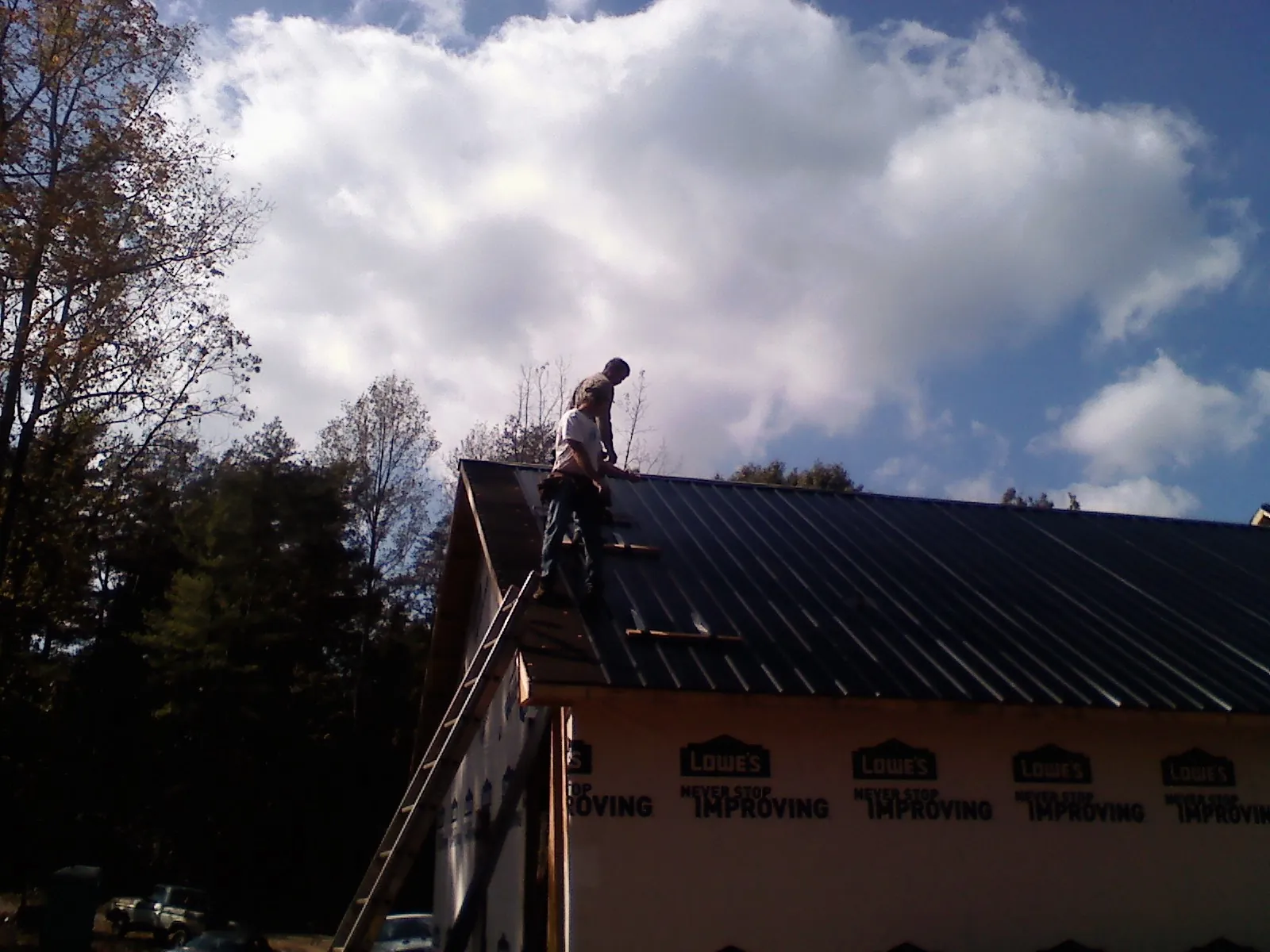 Roofer fastening dark metal panels high against a cloudy sky, from a Roof Inspection job in La Plata